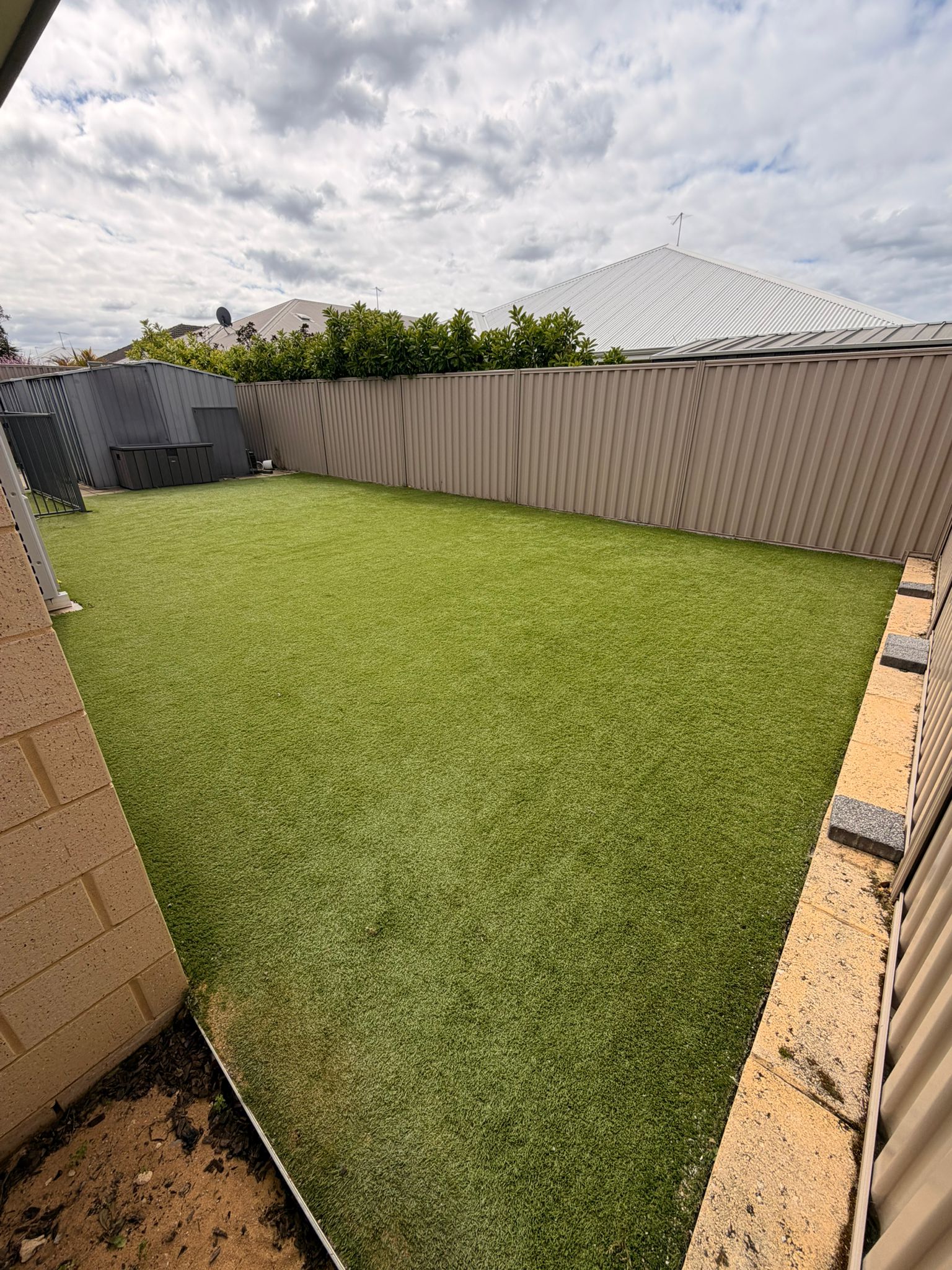 Established Beeliar backyard artificial lawn before cleaning, the pile dulled and flattened across the open middle of the yard on an overcast day